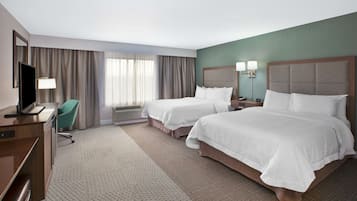 A hotel room with two beds, a desk with a chair, a television, and a large window with curtains.
