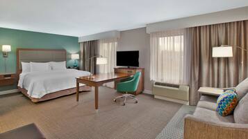 A hotel room with a bed, desk, chair, sofa, and TV.