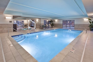 Une grande piscine intérieure avec des lignes de démarcation bien visibles pour les couloirs, un poste de surveillance pour les sauveteurs et un espace au bord de la piscine aménagé avec des chaises longues.