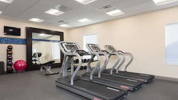 Un gimnasio con cintas de correr, un espejo y pelotas de ejercicio.