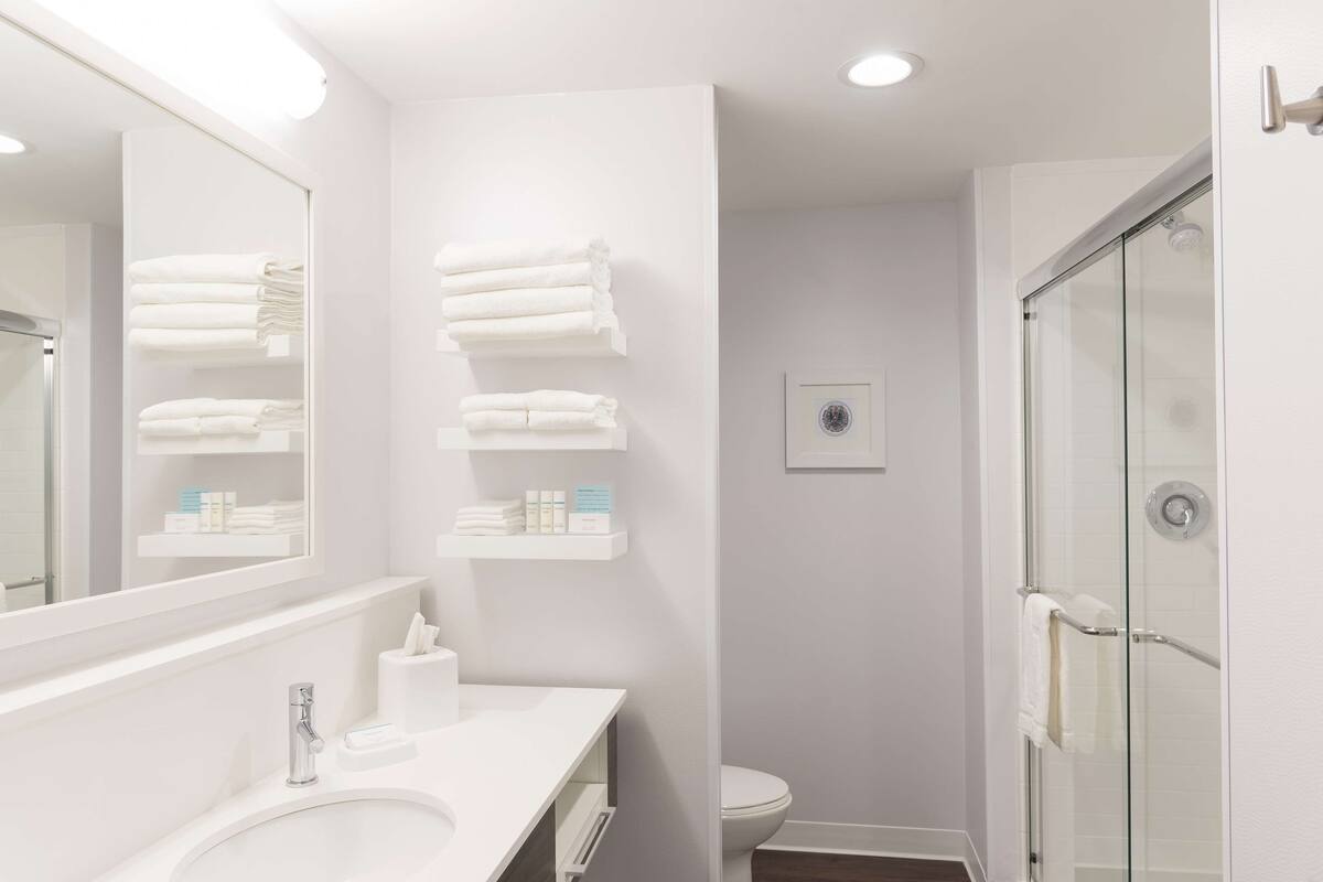 Une salle de bain moderne avec un grand miroir, un lavabo blanc et une douche à parois de verre.