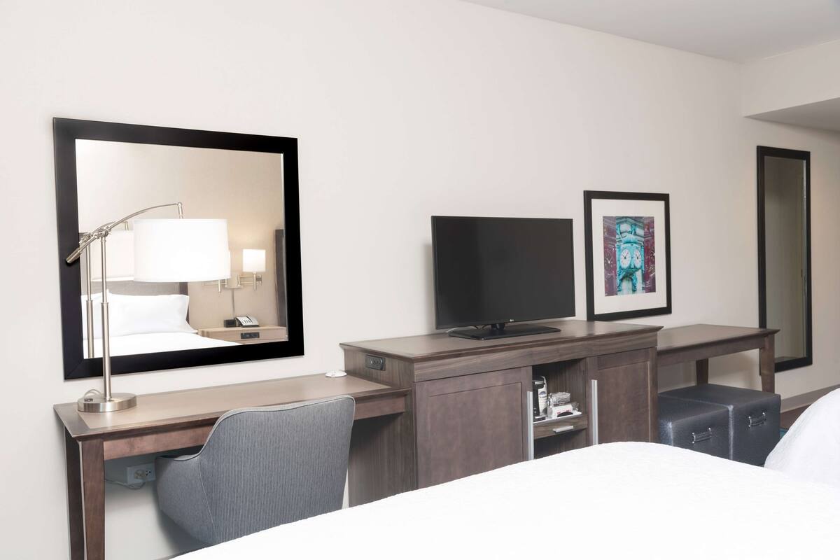 Une chambre d’hôtel avec un lit, un bureau doté d’une lampe, une télévision et un tableau encadré au mur.
