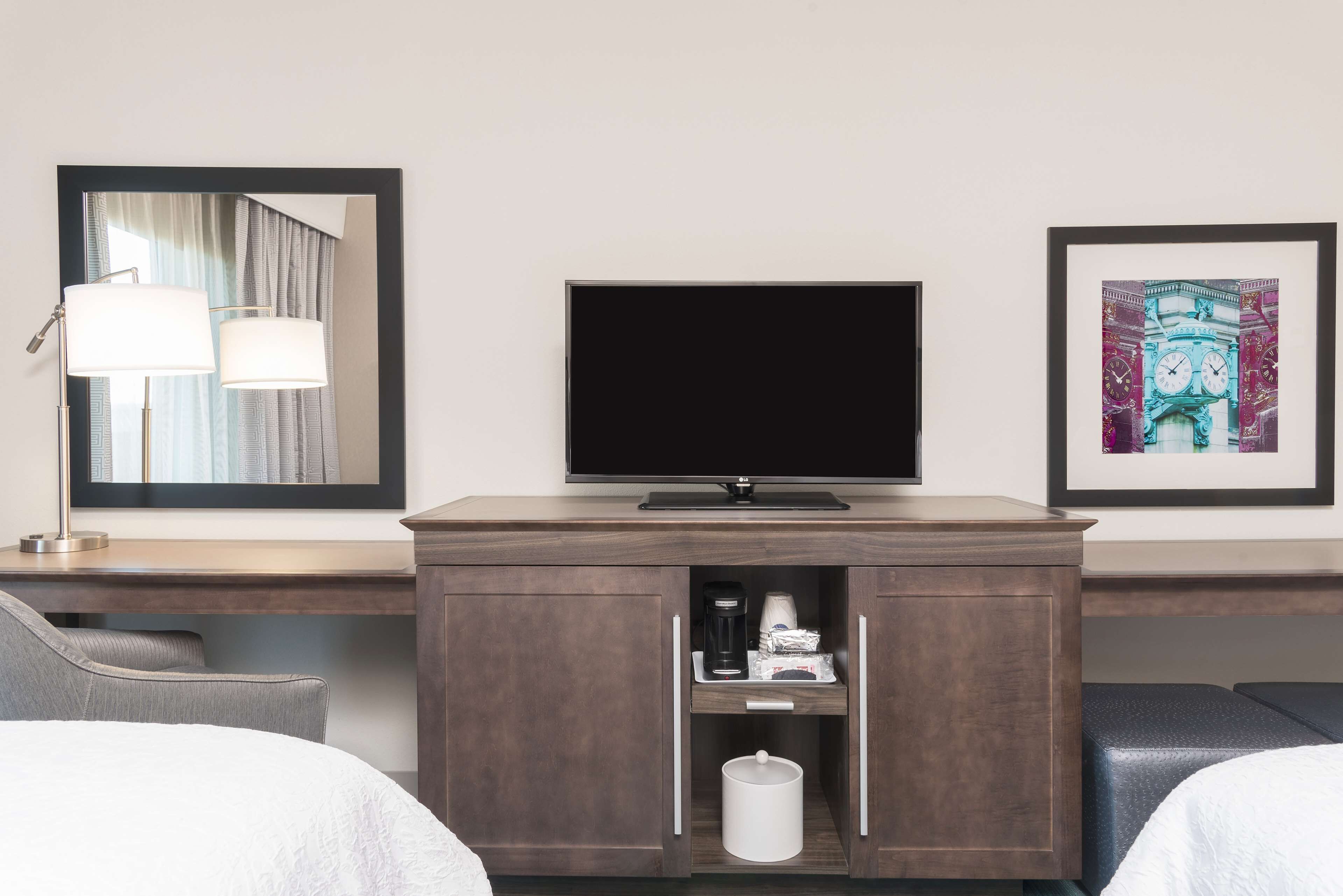 A hotel room with a bed, a desk with a lamp, a television, and a cabinet with a coffee maker.