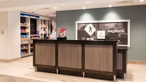 A hotel reception area with a modern design, featuring a reception desk, a sign that says "explore.", and a display of various snacks and beverages. - Hampton Inn & Suites Chicago Schaumburg (Schaumburg)