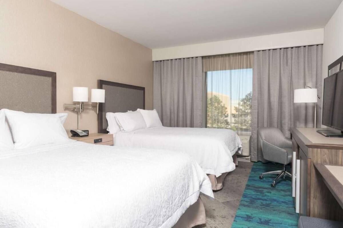 Une chambre d’hôtel avec deux lits, un bureau, une chaise, un téléphone et une fenêtre avec des rideaux.