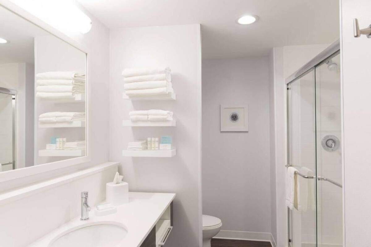 Une salle de bain moderne avec un grand miroir, un lavabo blanc et une douche à parois de verre.