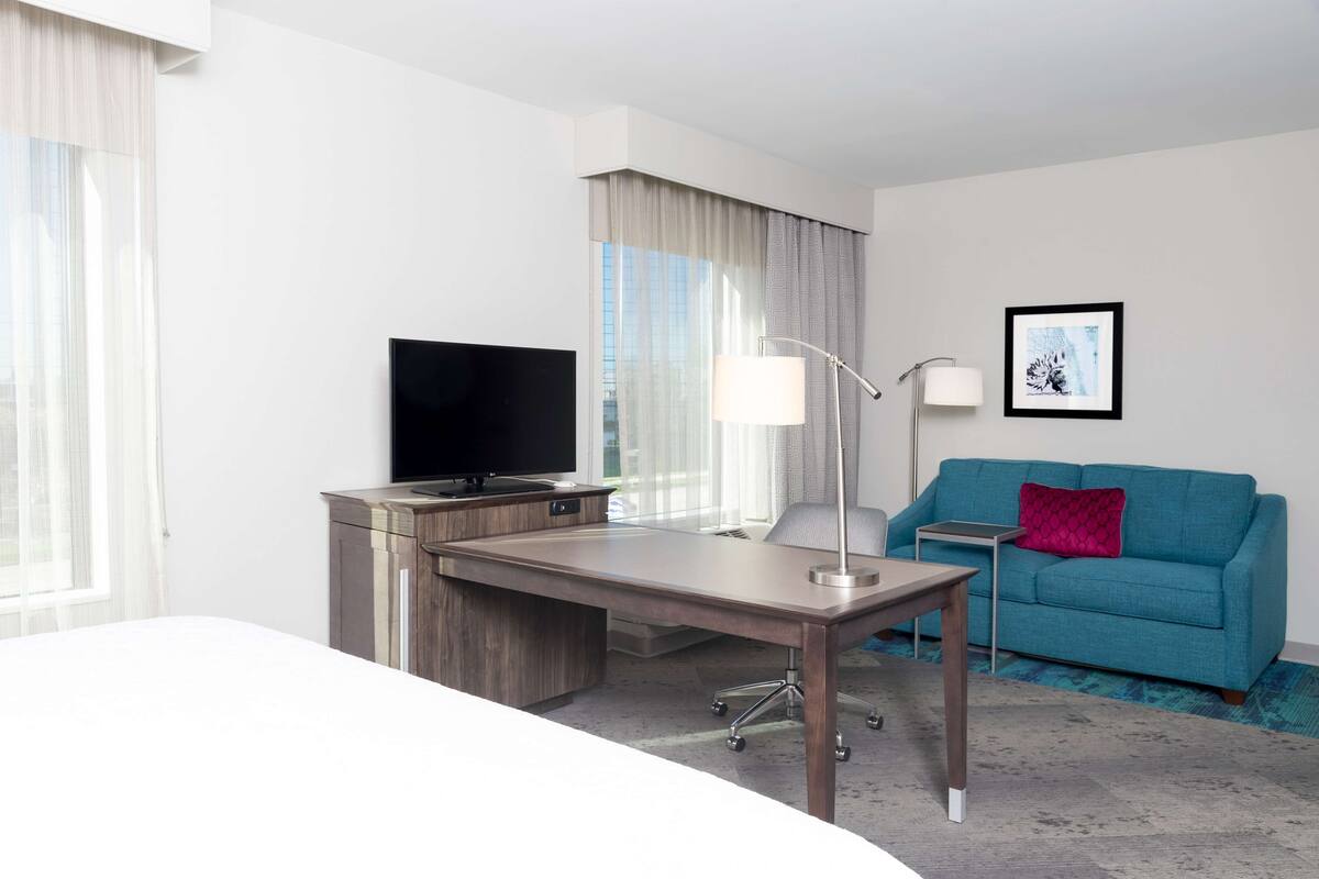 Une chambre d’hôtel équipée d’un bureau, d’une télévision, d’un canapé et d’un tableau encadré au mur.