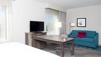 Una habitación de hotel con escritorio, televisión, sofá y un cuadro en la pared.