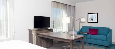 A hotel room with a desk, a television, a sofa, and a framed picture on the wall.