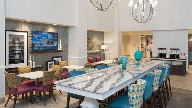 A modern dining area with a marble table, comfortable seating, a television, and a kitchen area in the background. - Hampton Inn & Suites Chicago Schaumburg (Schaumburg)