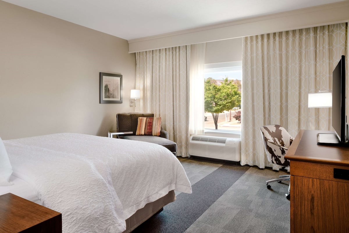 A hotel room with a large bed, a desk, a chair, a television, and a window with curtains.