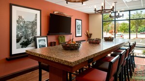 A kitchen with a granite countertop, a large island with bar stools, a flat-screen TV mounted above the island, and framed artwork on the walls. - Hampton Inn Kanab (Kanab)
