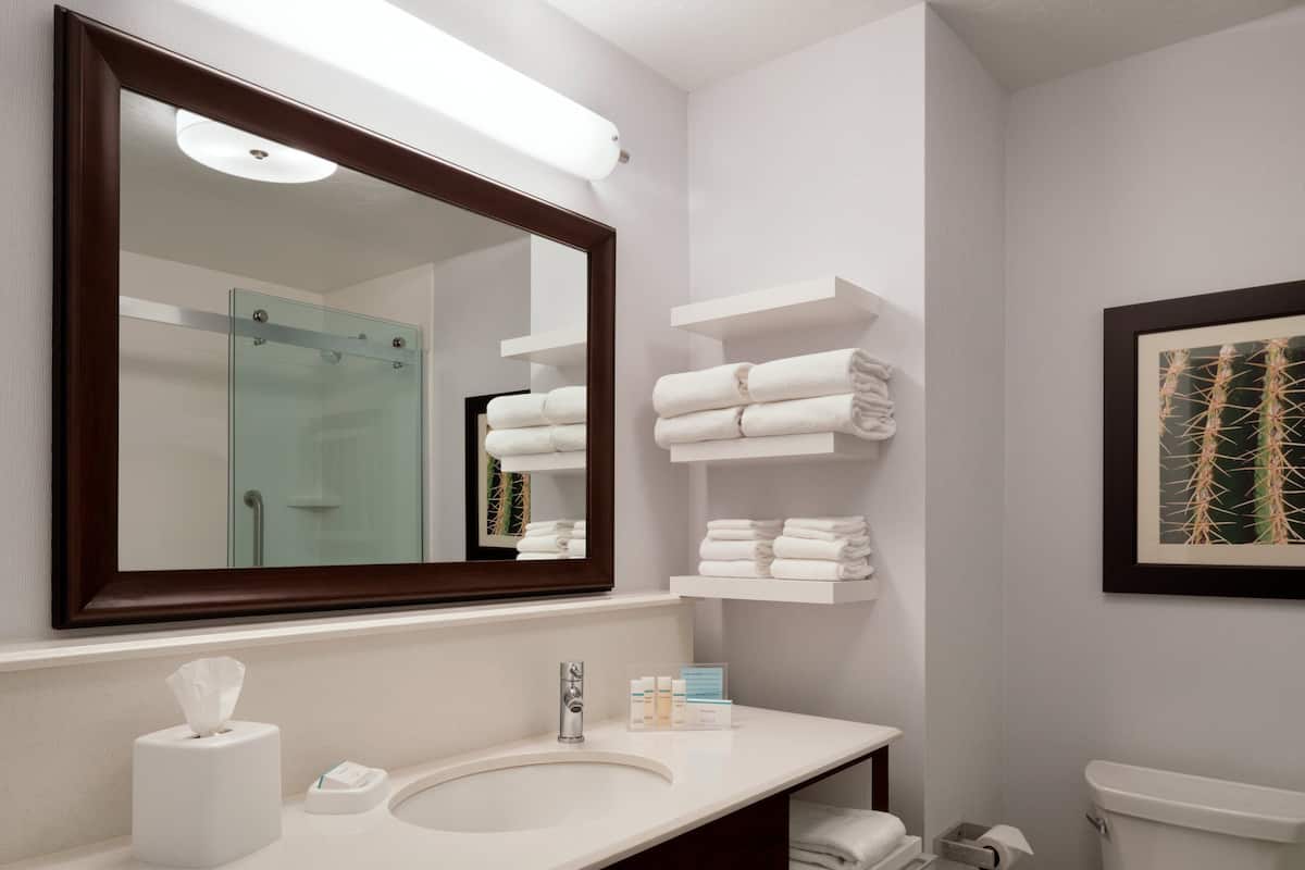 A modern bathroom with a large mirror, white sink, and neatly arranged towels.