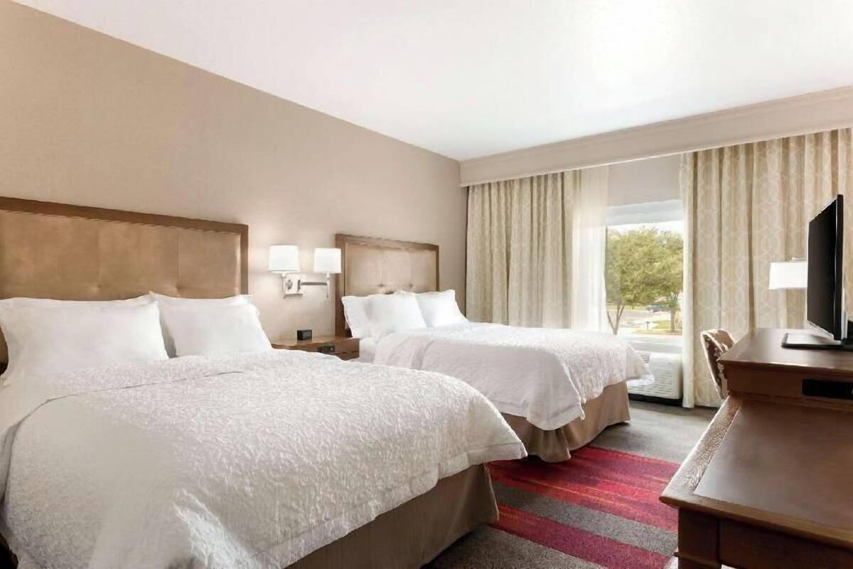 Une chambre d’hôtel avec deux lits, un bureau, une télévision et une fenêtre avec des rideaux.