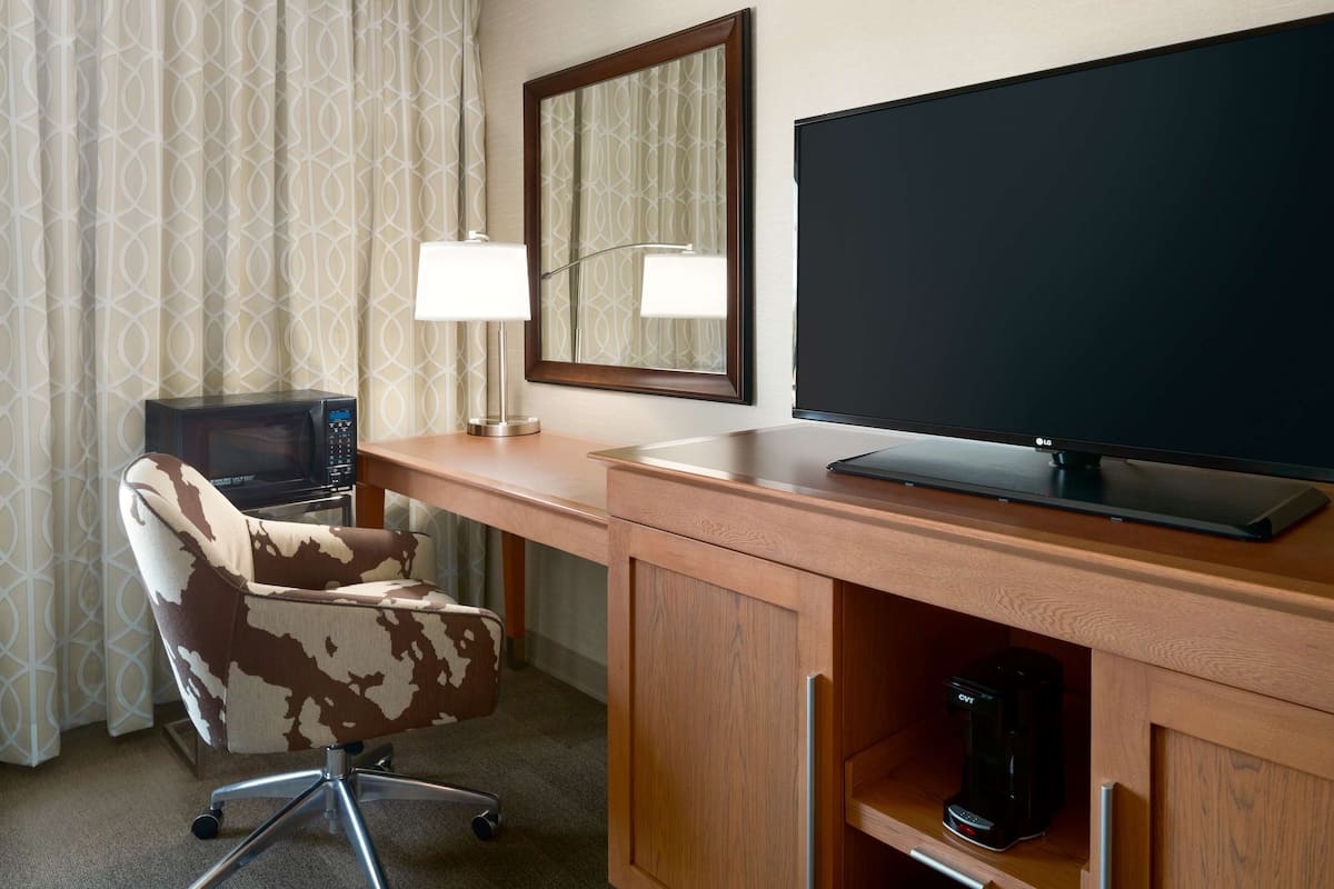 A hotel room with a wooden desk, a television, a coffee maker, and a patterned chair.