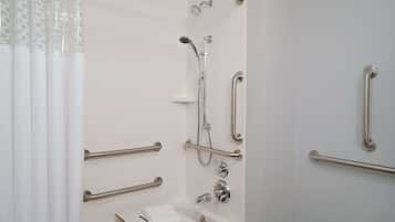 Un baño con ducha, barras de apoyo, lavamanos y toallero.