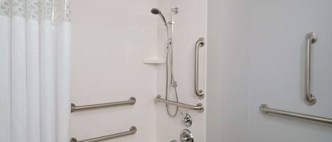 Une salle de bain équipée d’une douche, de barres d’appui, d’un lavabo et d’un porte-serviettes.