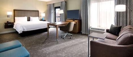 A hotel room with a bed, desk, chair, sofa, and a TV.