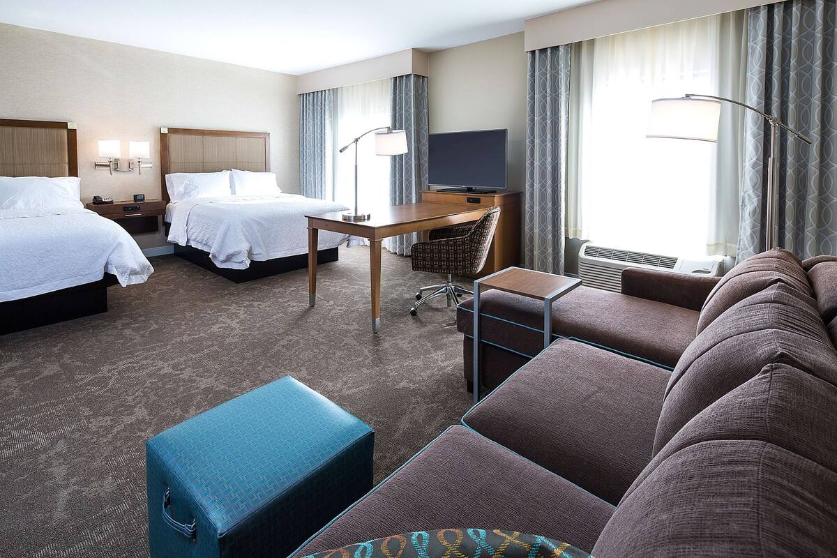 Quarto de hotel com duas camas, uma escrivaninha, televisão, sofá e uma poltrona.