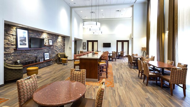 A spacious dining area with a long table and multiple chairs, a stone accent wall with framed pictures, and a flat-screen TV mounted above.