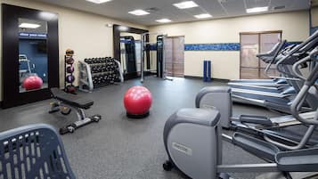 Un gimnasio con cintas de correr, pelotas de ejercicio, mancuernas y un banco.