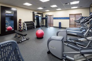Ein Fitnessraum mit Laufbändern, Gymnastikbällen, Kurzhanteln und einer Bank.