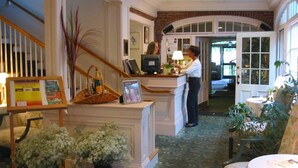 A reception area with a counter, a framed picture, a wicker basket, and potted plants. - The Governor's Inn (Rochester)