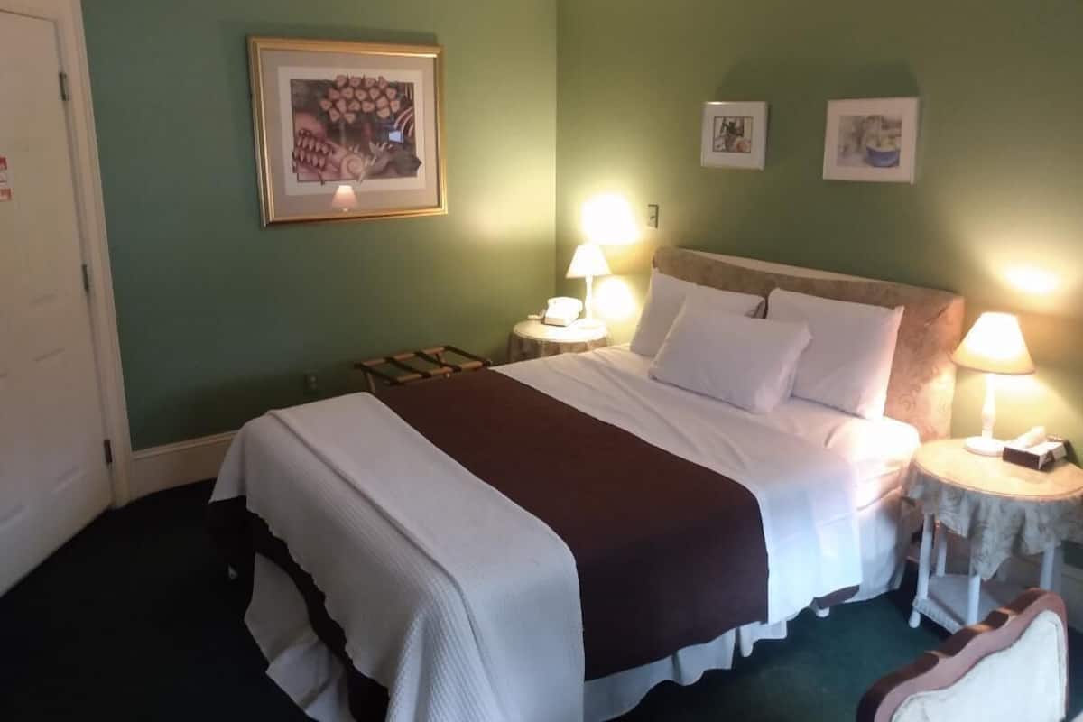 A hotel room with a large bed, two bedside tables with lamps, a framed picture on the wall, and a door.