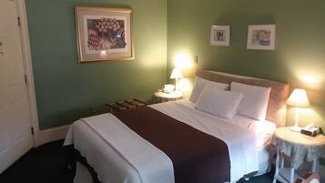 Une chambre d’hôtel avec un grand lit, deux tables de chevet avec des lampes, un tableau encadré au mur et une porte.