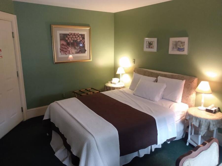 Une chambre d’hôtel avec un grand lit, deux tables de chevet avec des lampes, un tableau encadré au mur et une porte.