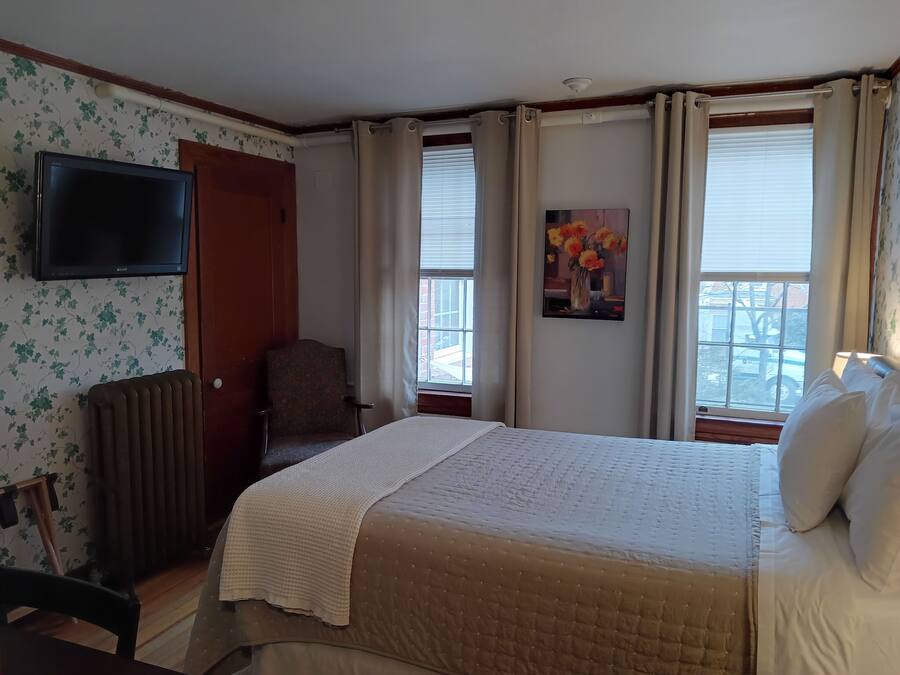 A hotel room with a bed, a chair, a radiator, a television, and a window with curtains.