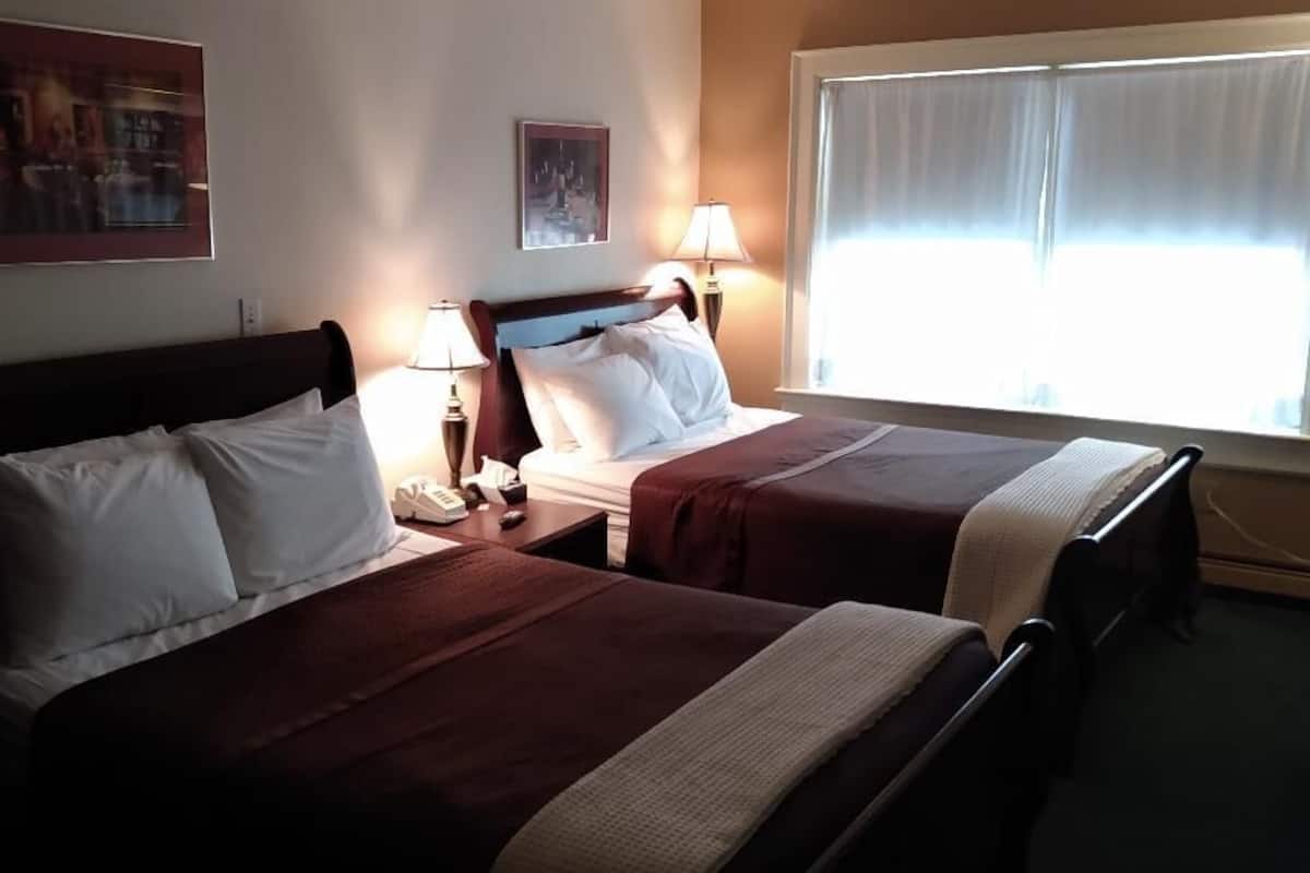A hotel room with two beds, a nightstand with a phone, two wall-mounted lamps, and a window with curtains.