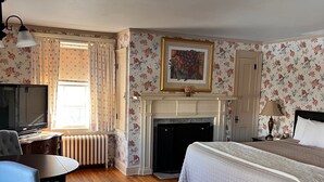 A hotel room with a bed, a desk, a chair, a fireplace, and a television. - The Governor's Inn (Rochester)