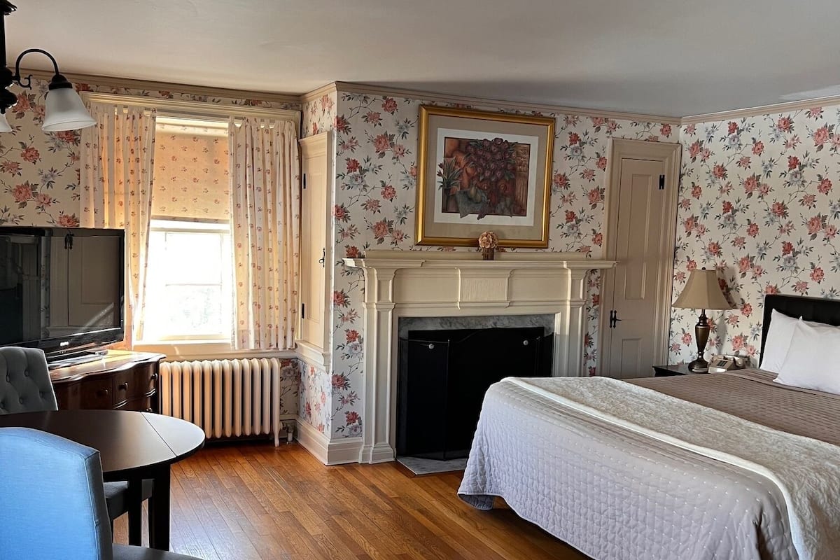 A hotel room with a bed, a desk, a chair, a fireplace, and a television.