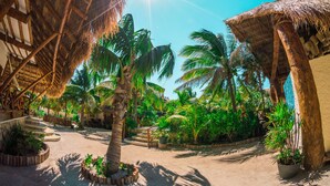 Um resort tropical com construções de palha, palmeiras e um pátio de areia.
