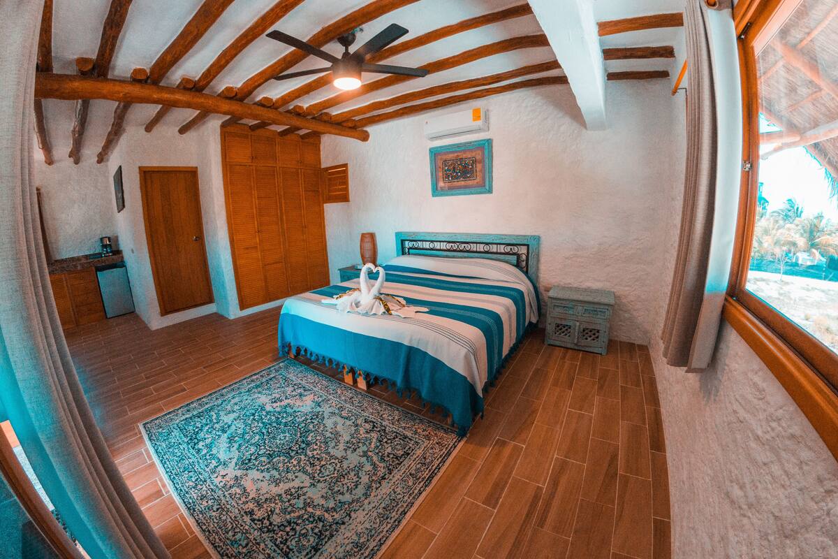 A bedroom with a bed, a wooden ceiling, a window, and a door.