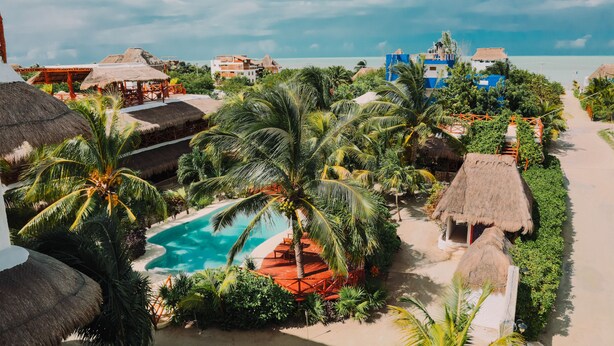 Um resort com piscina rodeada por palmeiras e construções com telhados de palha.