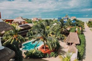 Ein Resort mit Swimmingpool, umgeben von Palmen und strohgedeckten Gebäuden.