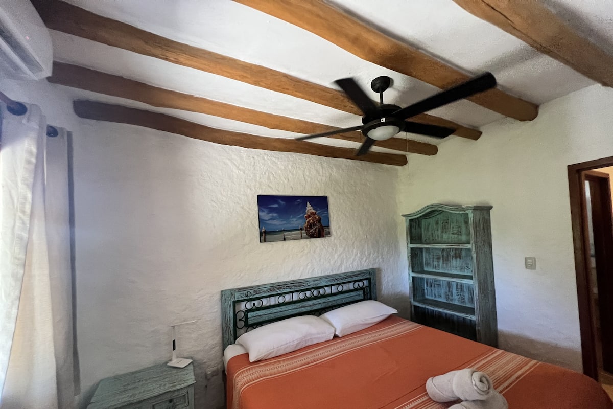 A bedroom with a bed, a ceiling fan, a painting, a wooden cabinet, and a nightstand.