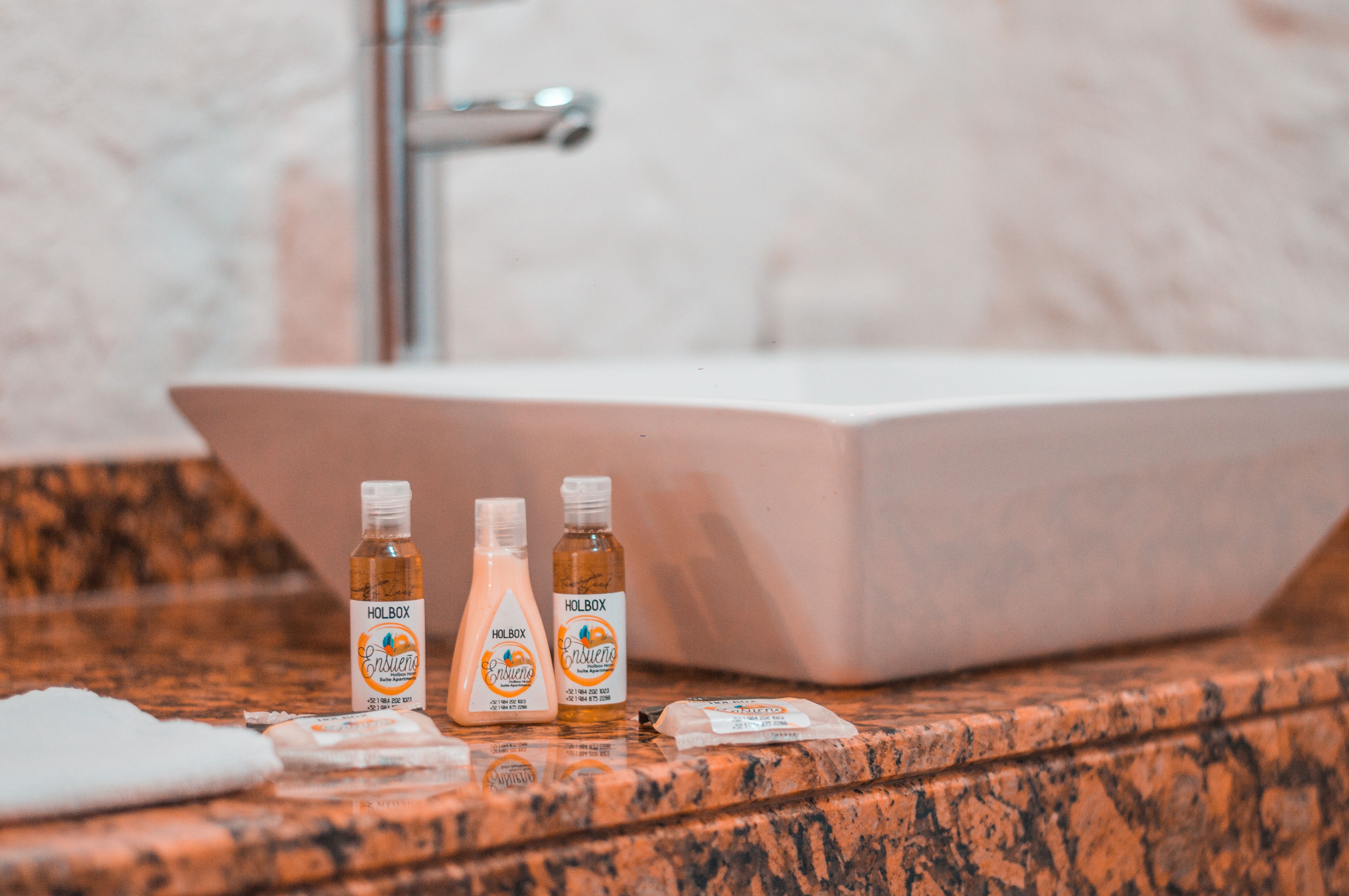 Une salle de bain avec un comptoir en marbre, trois bouteilles de gel douche Holbox Esencia et une serviette blanche.