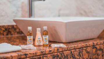 Une salle de bain avec un comptoir en marbre, trois bouteilles de gel douche Holbox Esencia et une serviette blanche.