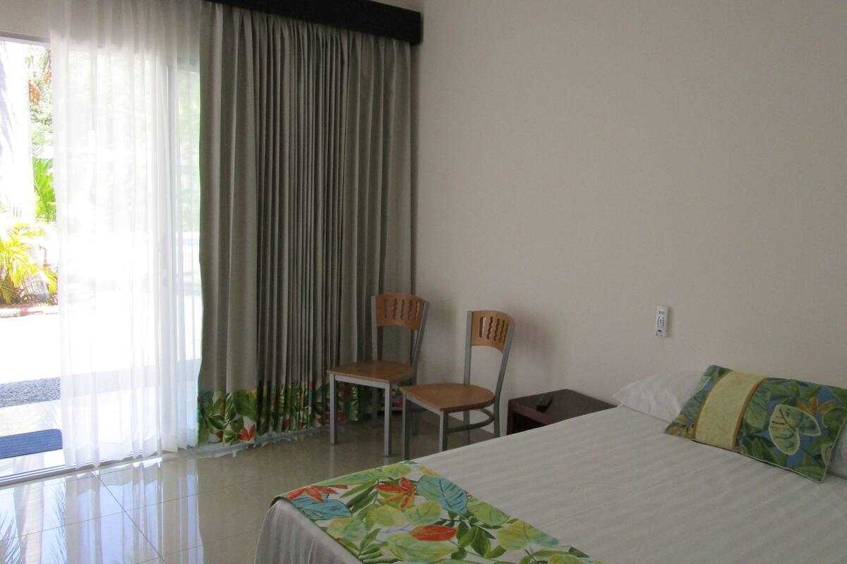 A hotel room with a bed, a chair, a nightstand, and a window with curtains.
