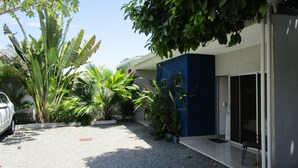Un edificio moderno con fachada azul, rodeado de plantas tropicales y un camino de grava.