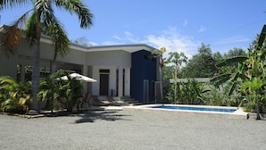 Un edificio moderno con piscina, rodeado de palmeras y otras plantas tropicales.