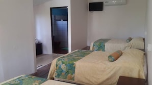 Habitación de hotel con dos camas, una mesita, un televisor instalado en la pared y un baño visible a través de una puerta abierta.