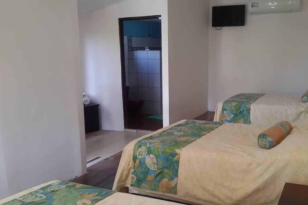 A hotel room with two beds, a small table, a TV mounted on the wall, and a bathroom visible through an open door.