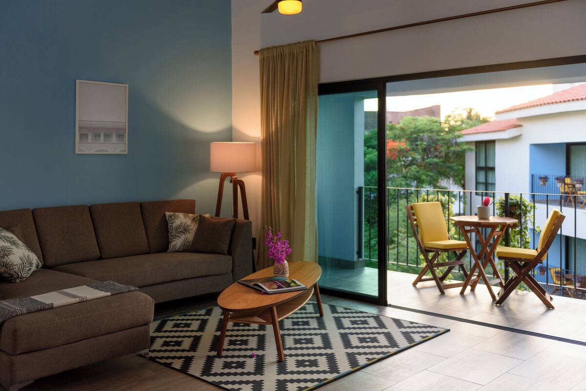 A living room with a sofa, coffee table, and a view of a balcony with chairs.