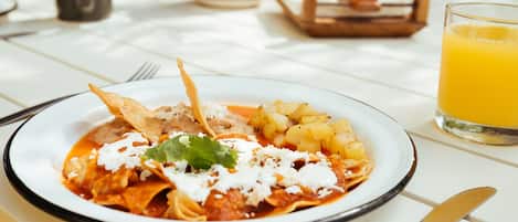 Una mesa de comedor con un plato de enchiladas, un vaso de jugo de naranja y un florero con flores.