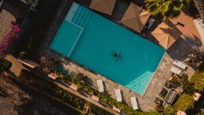 An aerial view of a rectangular swimming pool with a person swimming, surrounded by lounge chairs and umbrellas. - San Trópico Boutique Hotel & Peaceful Escape (Puerto Vallarta)