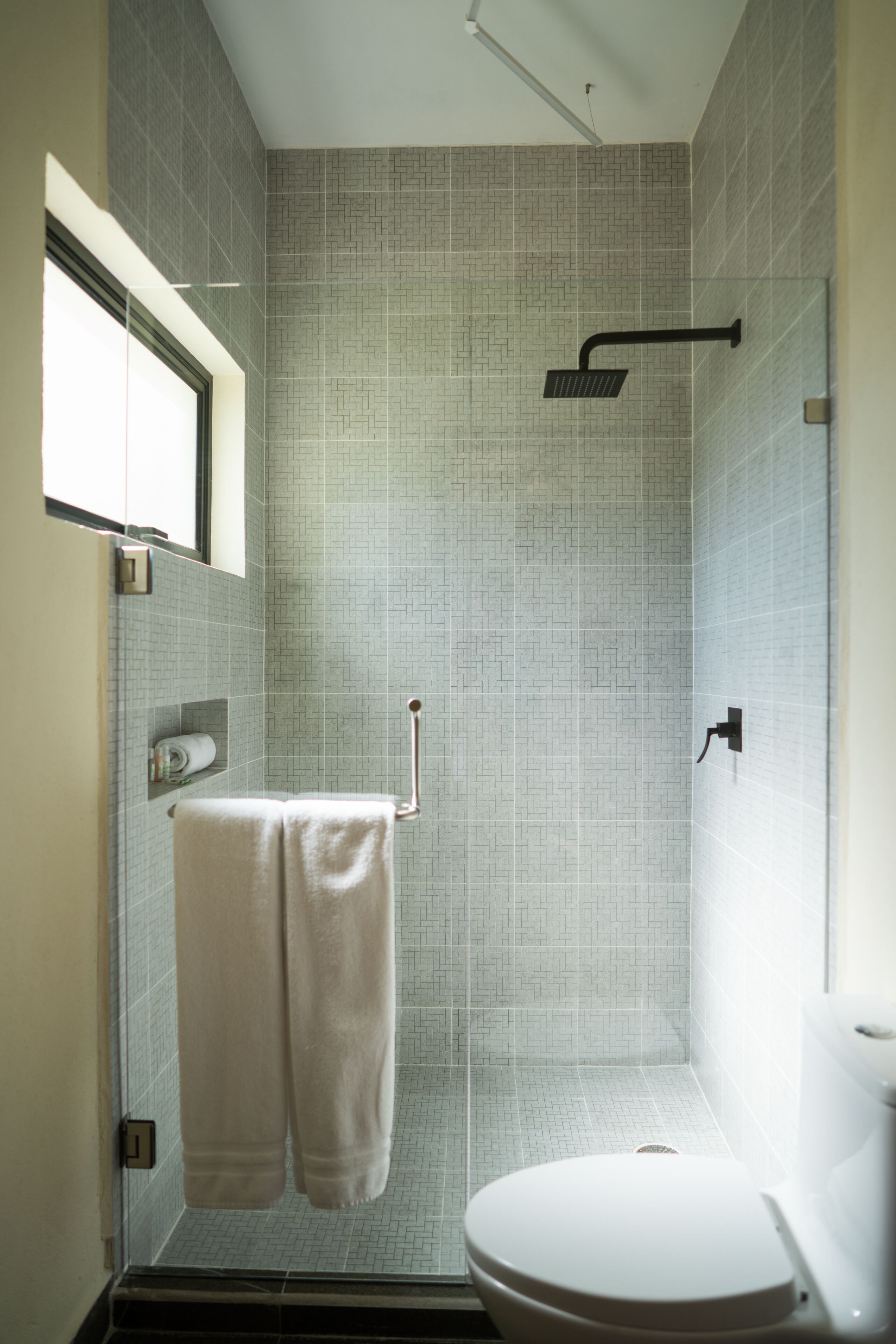 A small, modern bathroom with a shower, toilet, and a towel rack.